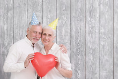 肖像快乐高级夫妇穿生日他持有红色的听到形状气球前面木背景