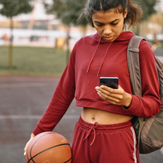 女人持有篮球在户外检查她的电话