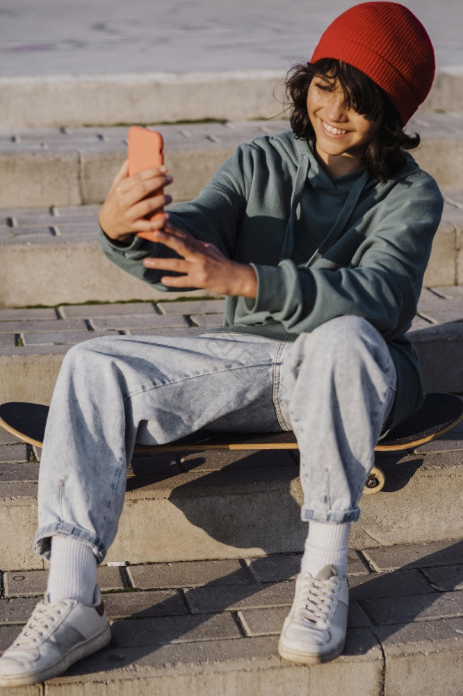 少年在户外坐着滑板采取自拍图片