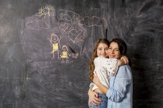 快乐妈妈。女儿拥抱附近黑板与画