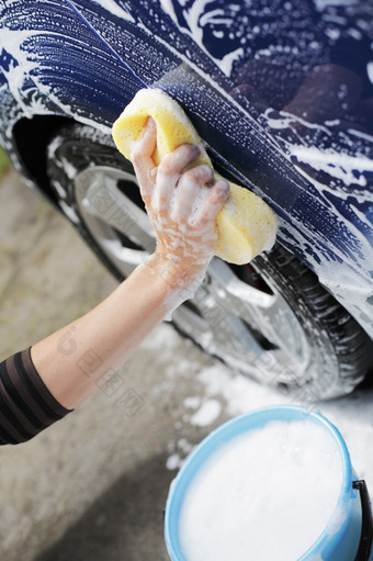 男人。洗蓝色的车与黄色的海绵而且桶肥皂水