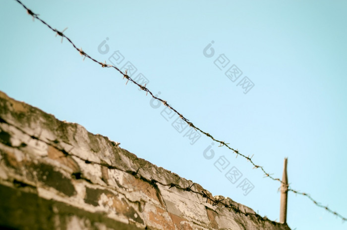 栅栏与有倒钩的线砖墙和蓝色的天空栅栏与有倒钩的线砖墙