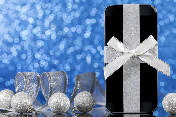 智能手机和装饰为圣诞节树黑色的玻璃表格在蓝色的背景焦点智能手机