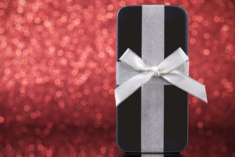 智能手机为圣诞节礼物黑色的玻璃表格在红色的背景焦点智能手机