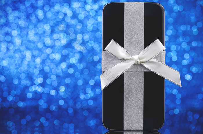 智能手机为圣诞节树黑色的玻璃表格在蓝色的背景焦点智能手机