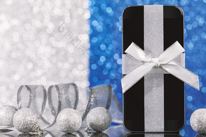 智能手机和装饰为圣诞节树黑色的玻璃表格在蓝色的和银背景焦点智能手机