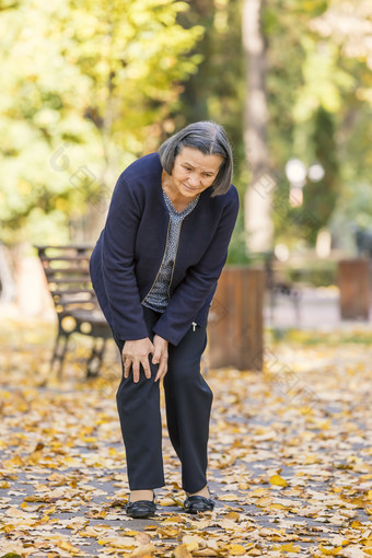 高级女人走秋天公园和有膝盖疼痛关节炎疼痛概念