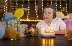 上了年纪的女人庆祝她的周年纪念日首页高级女人吹蜡烛生日蛋糕庆祝老化概念