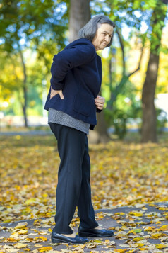 高级女人痛苦从背痛在户外秋天公园