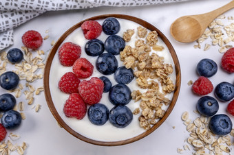 服务部分酸奶与<strong>蓝莓</strong>树莓和燕麦片木碗准备好了服务健康的食物为节食概念水果牛奶什锦早餐与酸奶