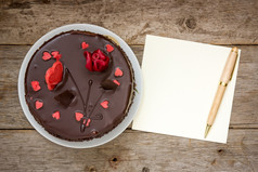 巧克力蛋糕与请注意纸而且笔的木背景