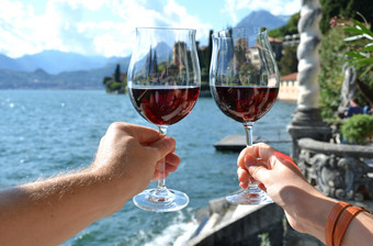 两个葡萄酒杯的手瓦伦纳小镇的湖作为意大利