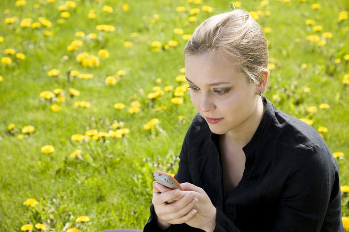 年轻的女人阅读短信的草地
