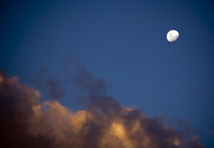 几乎完整的明亮的白色月亮上升在最后的光的云