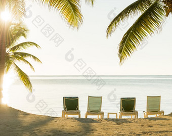 日落在热带海滩躺椅日落通过棕榈树在热带海滩与躺椅的沙子