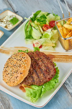 美味的烤汉堡白色板木表格与酱汁法国薯条和沙拉