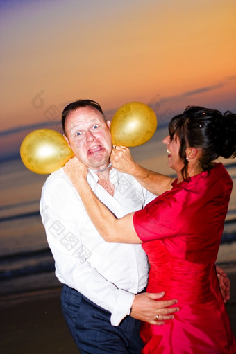 疯狂的新娘和新郎滑稽的婚礼时刻捕获前面海滩日落新结婚新娘假装扼杀和窒息她的新郎与气球