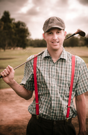 微笑经典复古的高尔夫球手穿平帽和<strong>背带</strong>裤持有他的高尔夫球俱乐部在他的肩膀过去的打高尔夫球球道去年