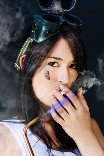 女机械师燕尾服持有乙炔火焰和吸烟香烟对它的蓝色的火焰粗糙的艰难的女概念上的