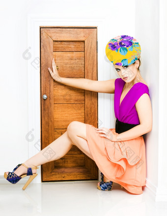 年轻的时尚的女人色彩鲜艳的时尚装蹲下来对墙与她的手臂和腿扩展出阻塞小门口时尚警察概念