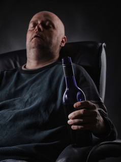 中间岁的男人。睡觉扶手椅而且持有酒瓶垂直格式