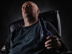 中间岁的男人。睡觉扶手椅而且持有酒瓶地平线格式