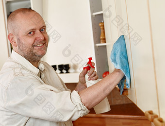作业微笑男人。使用清洁布而且洗涤剂喷雾清洁的厨房橱柜门