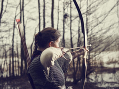 中世纪的弓箭手女人她穿链邮件而且使用弓而且箭头悲观的森林cross-processed图像