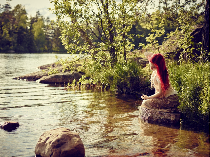 有吸引力的年轻的女人坐在的岩石而且她梦想夏天一天的湖