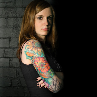 年轻的女与完整的手臂纹身倾斜对黑色的砖墙