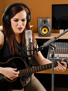 照片美丽的浅黑肤色的女人记录工作室玩声吉他而且唱歌成大隔膜麦克风