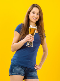 照片美丽的年轻的浅黑肤色的女人女人喝啤酒从高玻璃在黄色的背景