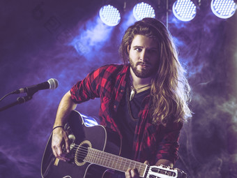照片年轻的男人。与长头发和胡子玩声吉他阶段与灯和音乐会<strong>大气</strong>