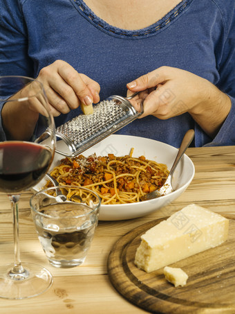 照片女人光栅帕尔玛奶酪在碗传统的意大利面肉酱与玻璃红色的酒