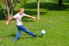 年轻的男孩玩与他的球的草在户外