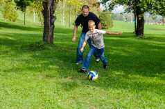 年轻的男孩玩足球与他的父亲在户外