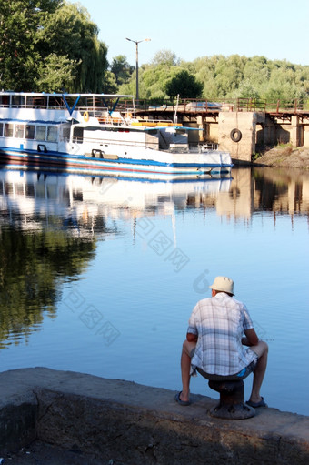 渔夫钓鱼的城市河附近电动机船渔夫坐着而且钓鱼的城市河附近电动机船