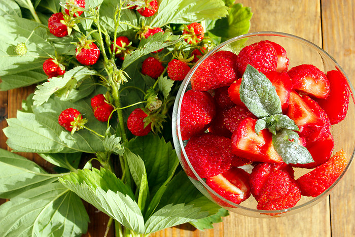草莓碗和草莓束切片成熟的草莓透明的碗和草莓束与叶子浆果的棕色（的）背景