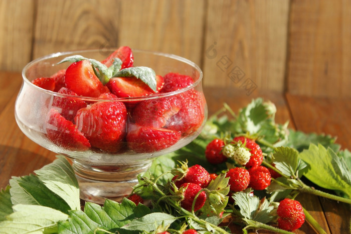 成熟的草莓透明的碗和束与叶子切片成熟的草莓透明的碗和草莓束与叶子