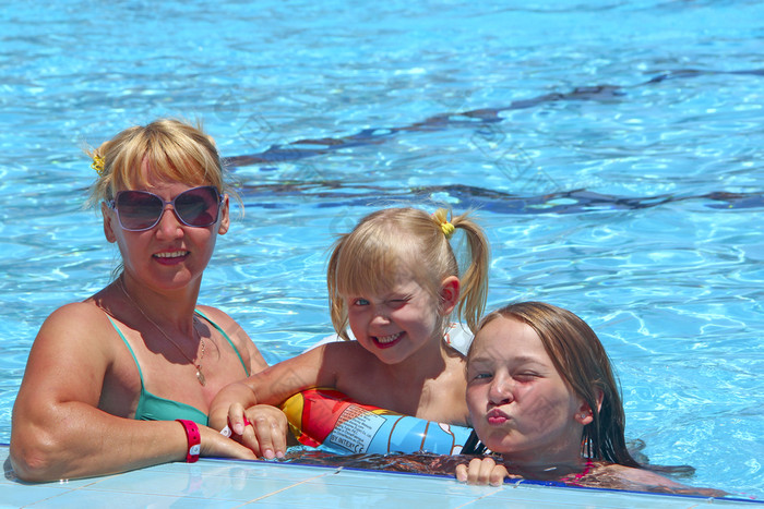 快乐妈妈。与她的女儿坐着游泳池摆姿势前面相机快乐家庭团队家庭享受夏天假期人享受家庭假期女团队快乐妈妈。与她的女儿坐着游泳池摆姿势前面相机