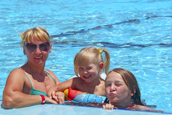 快乐妈妈。与她的女儿坐着游泳池摆姿势前面相机快乐家庭团队家庭享受夏天假期人享受家庭假期女团队快乐妈妈。与她的女儿坐着游泳池摆姿势前面相机