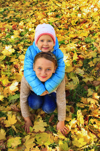 年轻的漂亮的姐妹坐和拥抱黄色的叶子秋天公园小蔡尔兹与秋天叶子小女孩秋天森林秋天的情绪秋天的走快乐童年年轻的漂亮的姐妹坐和拥抱黄色的叶子秋天公园