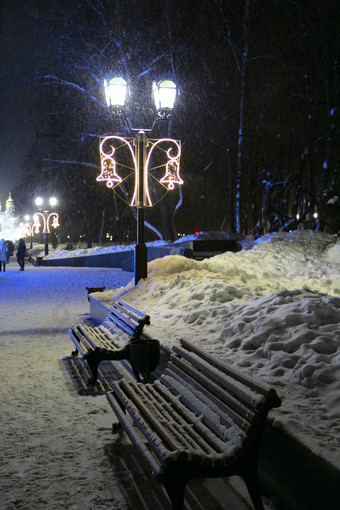 长椅白雪覆盖的公园长椅城市公园与美丽的圣诞节灯笼和雪地里照明城市公园在新一年假期长椅城市公园与美丽的圣诞节灯笼和雪地里