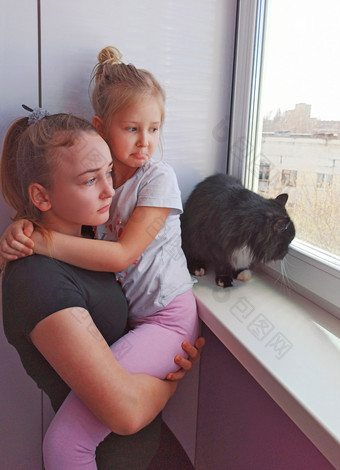 <strong>伤心</strong>孩子们和黑色的猫看出窗口在检疫孩子们想要走外冠状病毒检疫概念<strong>伤心</strong>姐妹和猫窗台支出时间在检疫女孩在一起与猫看可悲的是出窗口住首页在检疫