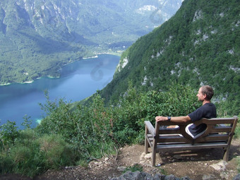孤独的男人。欣赏山景观而坐着板凳上的家伙休息山的家伙看景观与山和湖旅行者有休息山旅游斯洛维尼亚语阿尔卑斯山脉孤独的男人。欣赏山景观而坐着板凳上