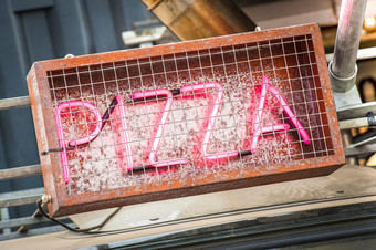 粉红色的霓虹灯披萨标志内部生锈的金属笼子里