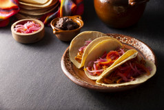 炸玉米饼科奇尼塔pibil典型的墨西哥炖肉从尤卡坦半岛使从猪肉腌制与胭脂树的种子和一般陪同与豆子和红色的洋葱与哈瓦那辣椒