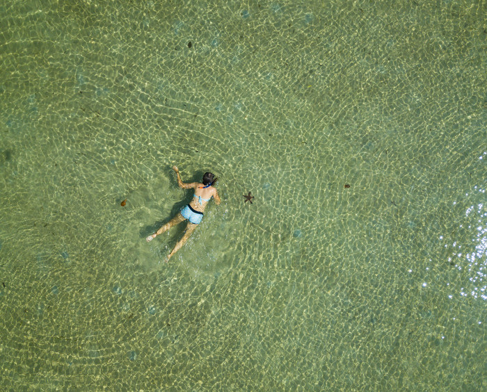 的空中视图游泳女人水夏天海景与女孩清晰的Azure水波日出透明的水前视图从飞行无人机空中视图游泳女人水夏天海景与女孩清晰的Azure水波日出透明的水前视图从飞行无人机