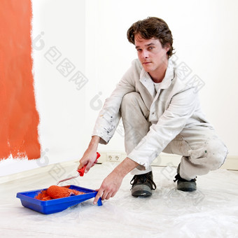 画家跪着下来续杯他的油漆辊与橙色油漆同时重新装修房间