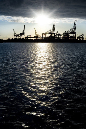 轮廓工业港口对明亮的日落反映了的黑暗冷水